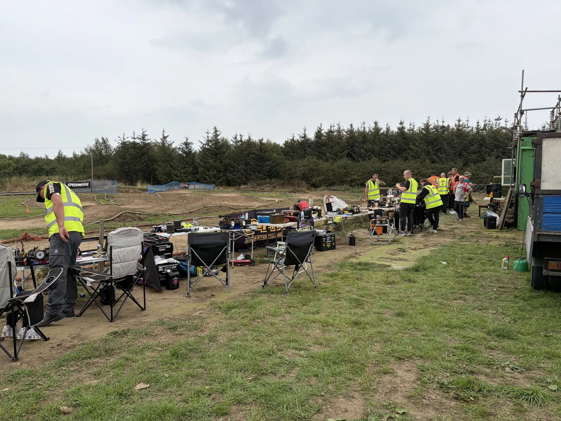 Racers working on RC cars at pitting tables alongside the dirt track